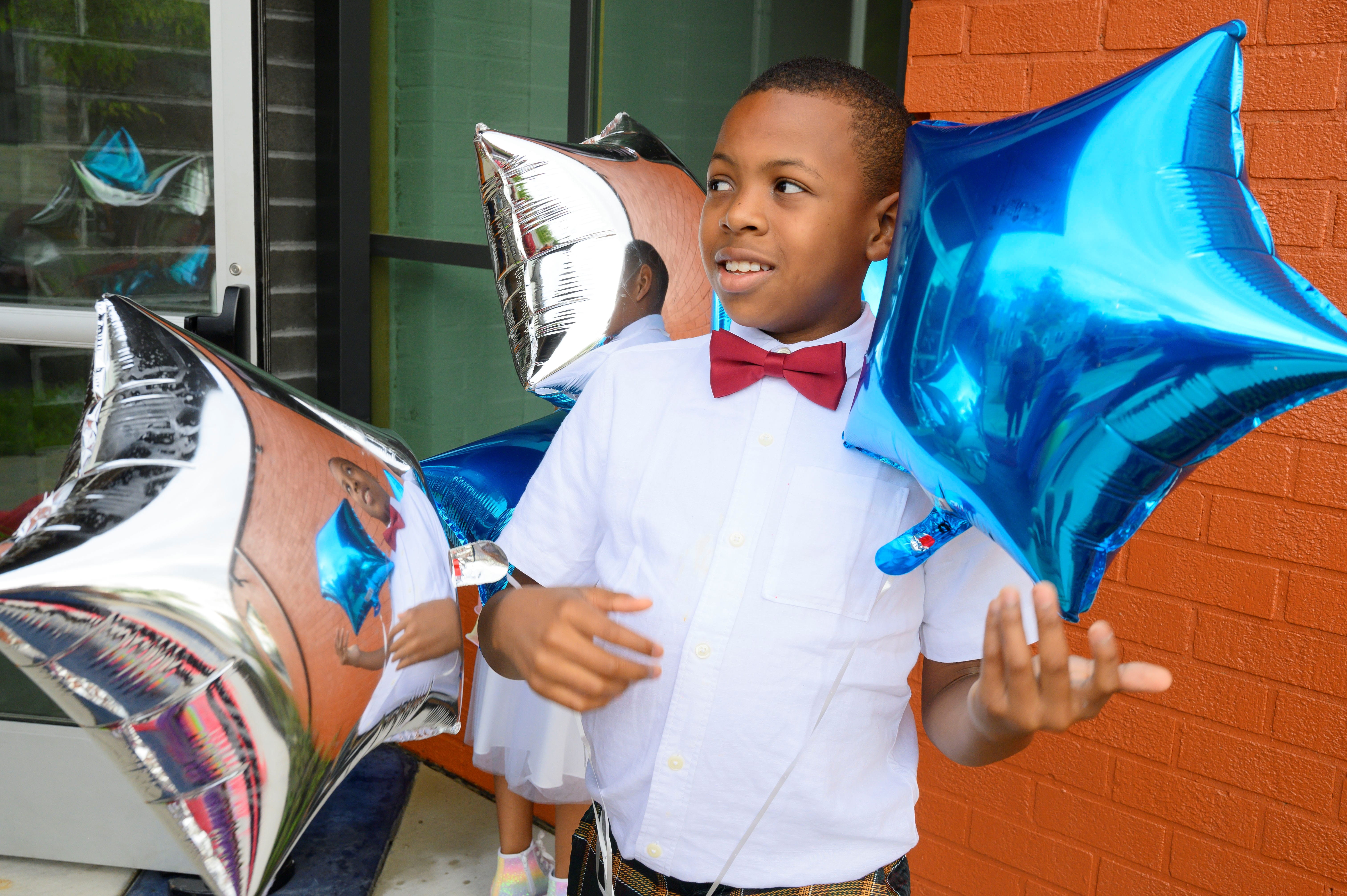 young participant of Bon Secours Community Works sneaker ball poses with several star shaped balloons