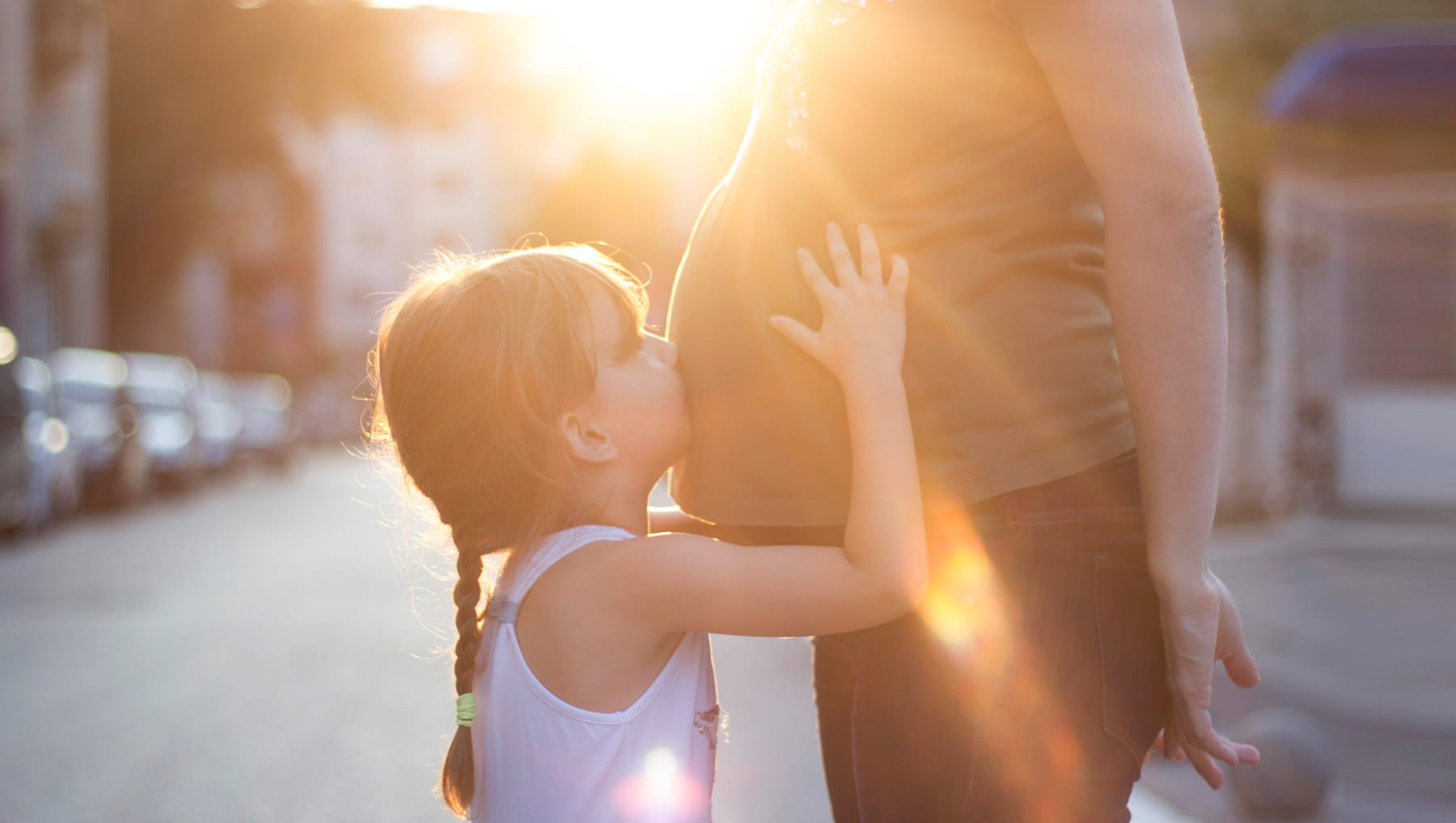 child kissing her pregnant mother's belly
