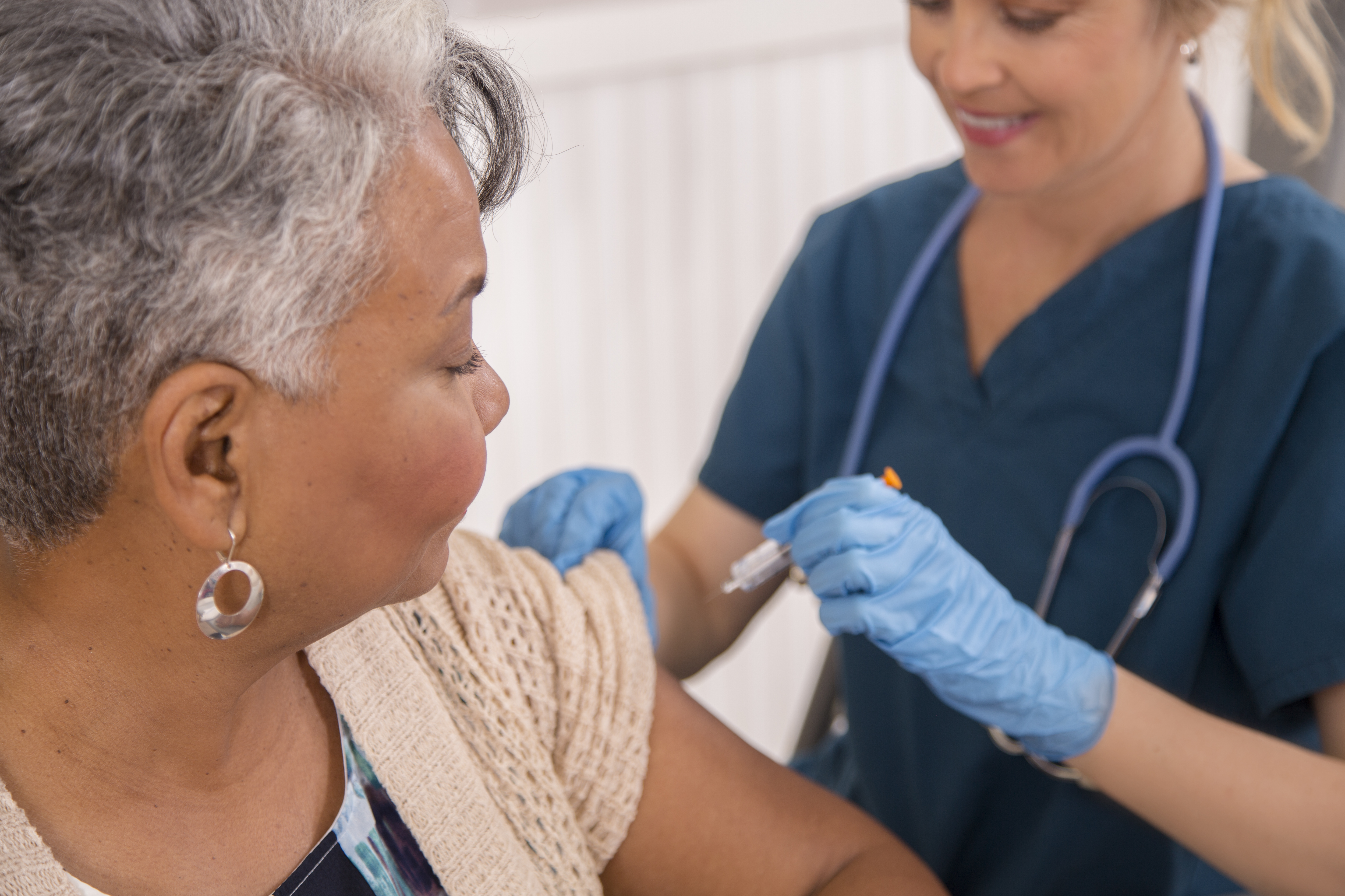 Nurse gives flu vaccine to African descent, senior adult patient at a local pharmacy, clinic, or doctor's office