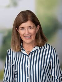 Head shot of Susan Collett, female wearing a vertically striped shirt has medium length brown hair.