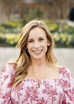 Head shot of woman in floral top, long hair. Picture was taken outside in a garden setting.